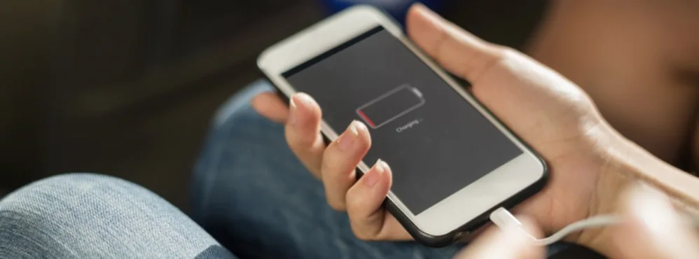 Person holding a smartphone showing a red low-battery icon while it charges